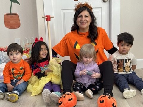 Antonia in an orange pumpkin shirt sitting on the floor with four children in costumes