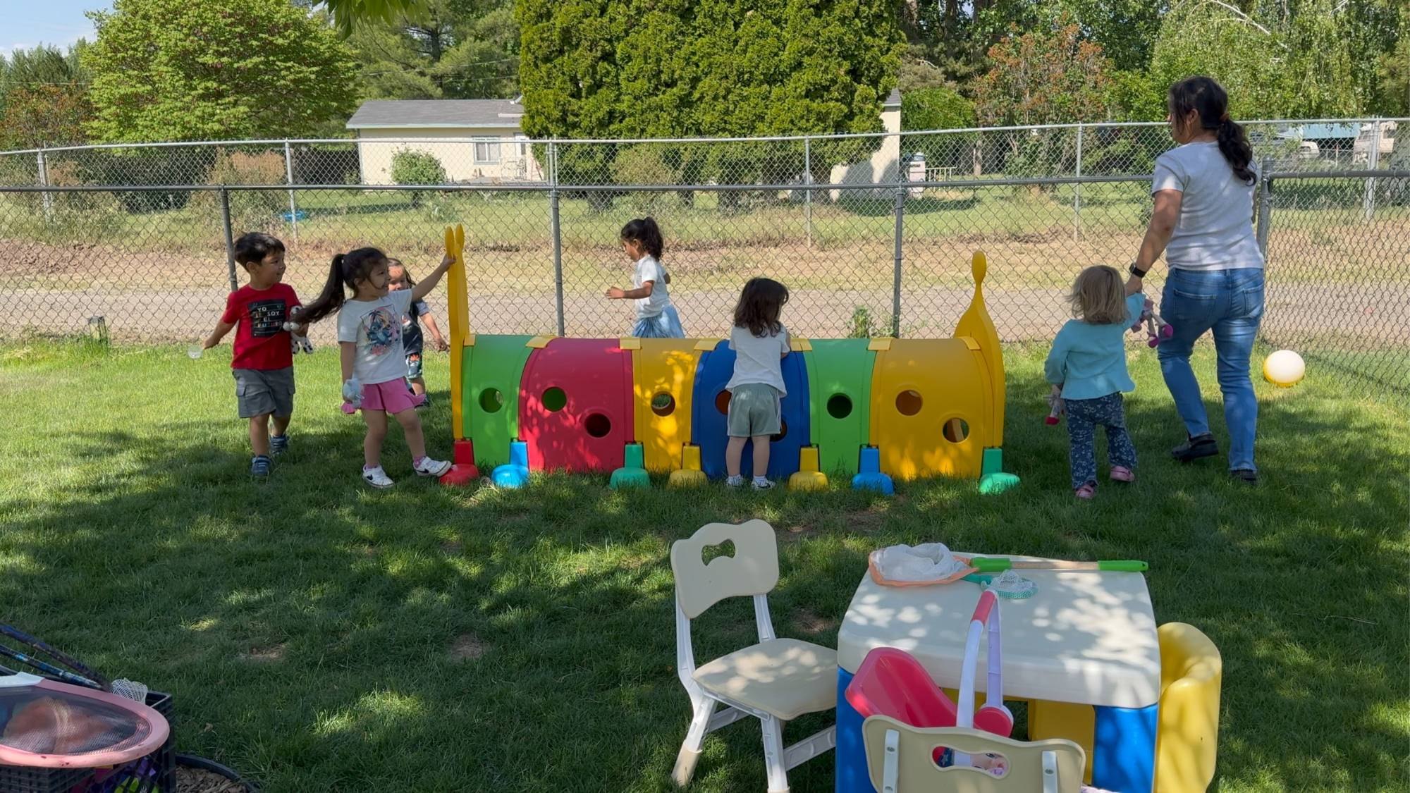 Antonia playing with a group of children around a caterpillar tunnel in the backyard