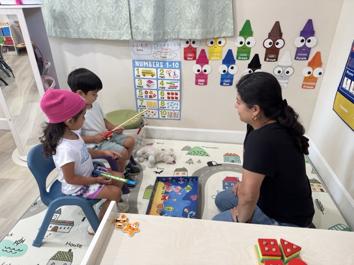 A teacher sitting on the floor with two children playing a fishing game