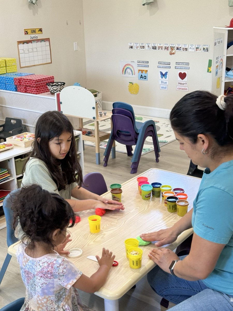 Two girls and a teacher with cups of play-dough